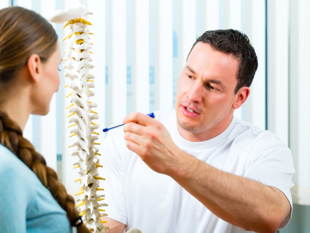 Chiropractor in Brooklyn explaining a spine model to a patient in a clinic, highlighting workplace wellness and spinal care.
