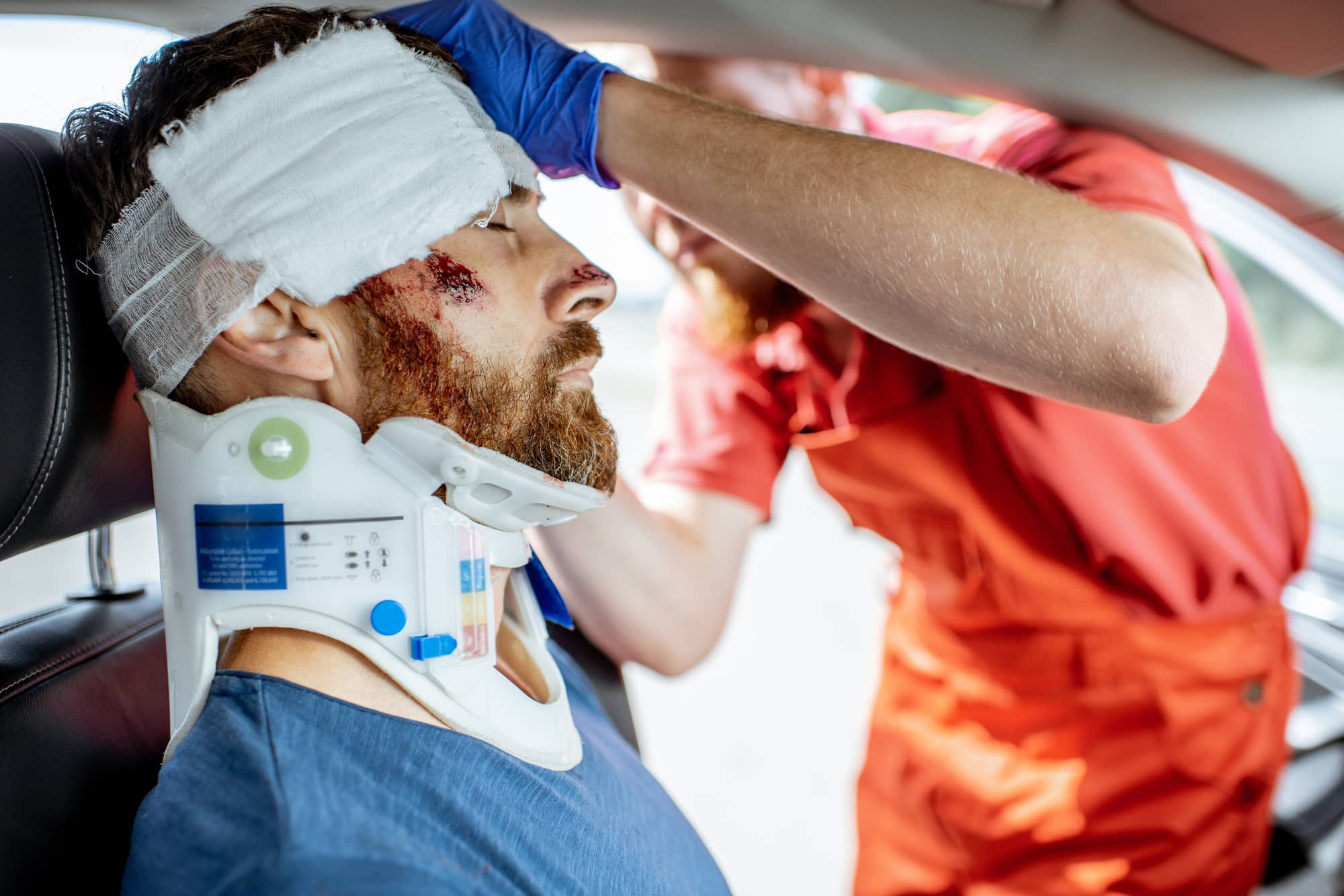 Médico aplicando un vendaje en la cabeza de una víctima con graves daños sentada en el asiento del conductor tras el accidente de tráfico. Prestando asistencia médica de urgencia